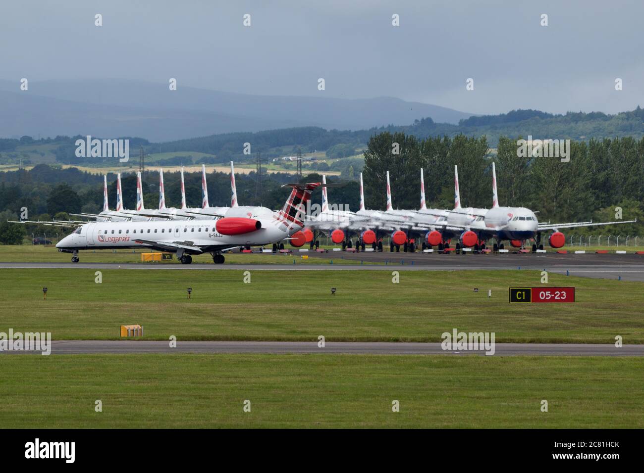 Glasgow, Schottland, Großbritannien. Juli 2020. Im Bild: Loganair Embraer ERJ145 Flugzeug gesehen am Flughafen Glasgow mit einer großen Gruppe von geerdeten British Airways (BA) airbus-Flugzeugen im Hintergrund. Loganair hatte einige Zeitnischen von Flybe nach dem Zusammenbruch von Flybe übernommen, dann traf die Coronavirus-Sperre im März, und seitdem hat Loganair die Dienste erhöht, aber dies sind turbulente Zeiten für alle Fluggesellschaften und die globale Luftfahrtindustrie. Quelle: Colin Fisher/Alamy Live News Stockfoto