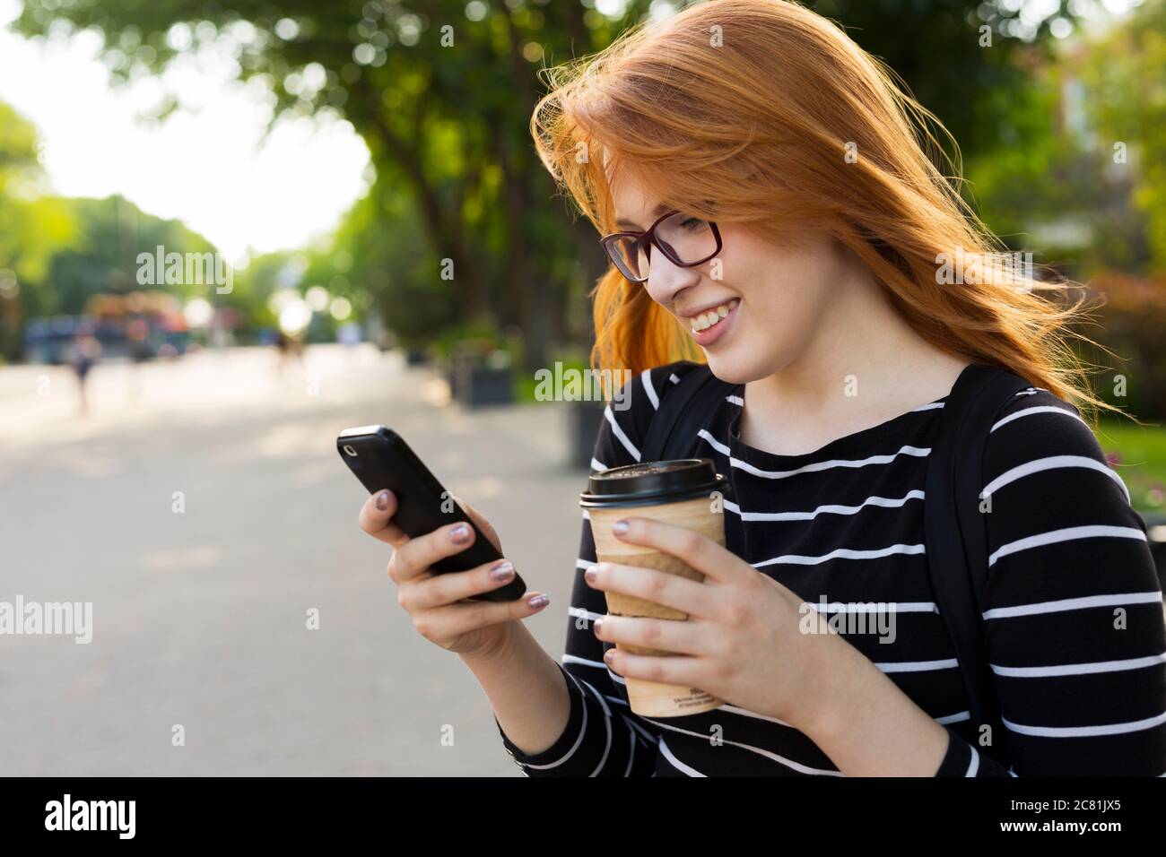 Eine junge Studentin steht mit einer Kaffeetasse und ihrem Smartphone auf dem Campus in Edmonton, Alberta, Kanada Stockfoto