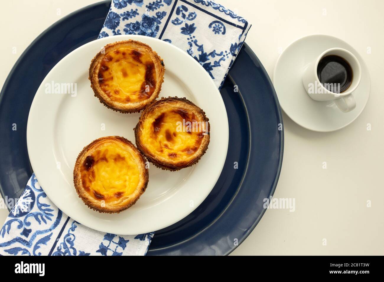 Portugiesische Pastel de Nata Kustentarttörtchen und Espresso Kaffee mit portugiesischem Design Tuch Serviette auch bekannt als Pastéis de Nata Pastéis de Belém Pastel Stockfoto