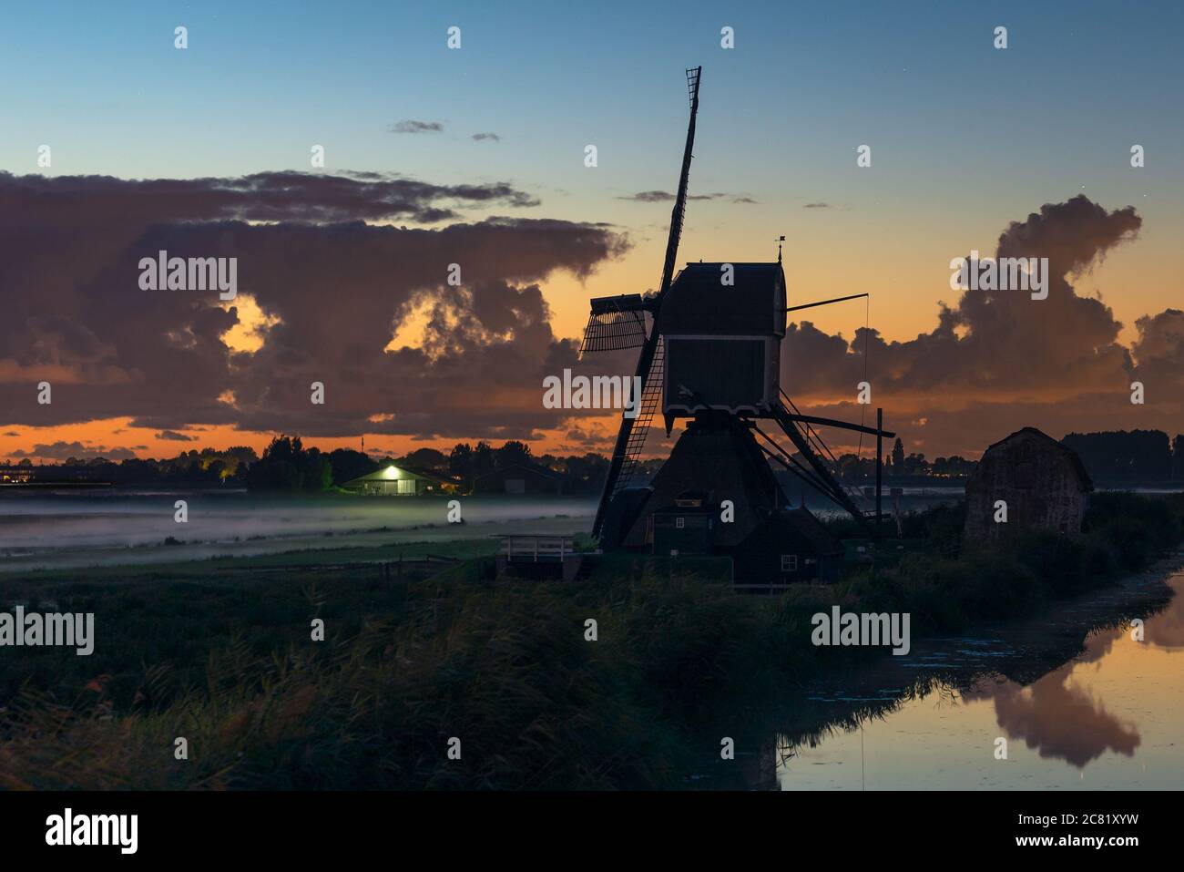 Traditionelle holländische Windmühle bei Sonnenuntergang mit Nebel über den Wiesen Stockfoto