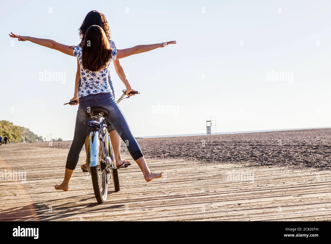 Zwei Freunde reiten Tandem auf einem Fahrrad zusammen mit barfuß auf einer Holzboardwalk entlang Woodbine Beach; Toronto, Ontario, Kanada Stockfoto
