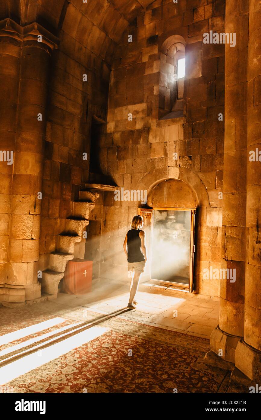 Junge Dame auf dem Weg zum Licht. Die Kraft des Lichts. Lichtstrahl. Geheimnisvolle ruhige Atmosphäre. Mädchen in einer Kirche. Altes armenisches Steinkloster mit Stockfoto