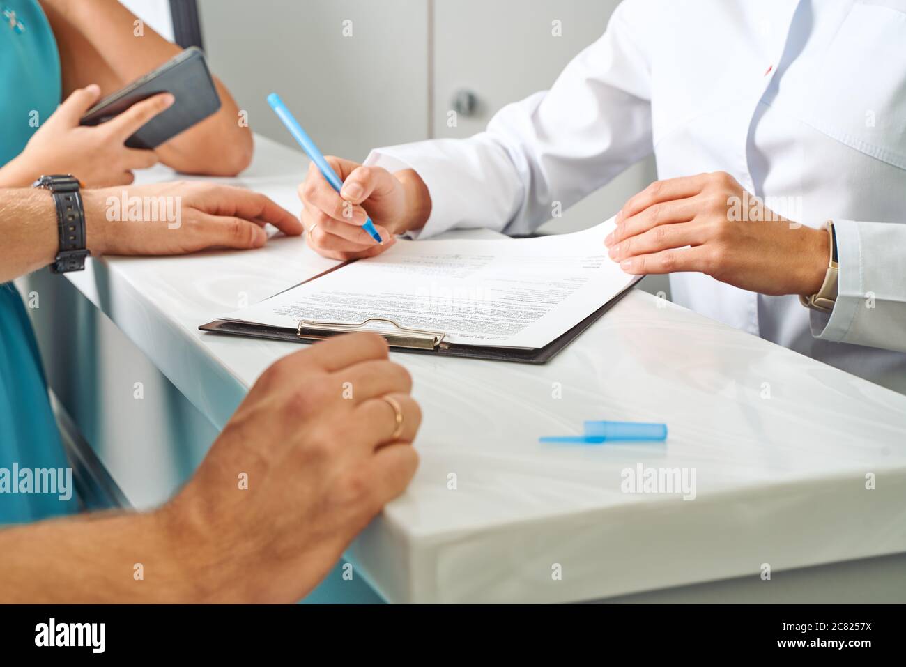 Teilweise Ansicht des Arztes im weißen Mantel, der Notizen in Notizblock mit weiblicher Patientin in der Nähe während des Termins in der Klinik macht Stockfoto