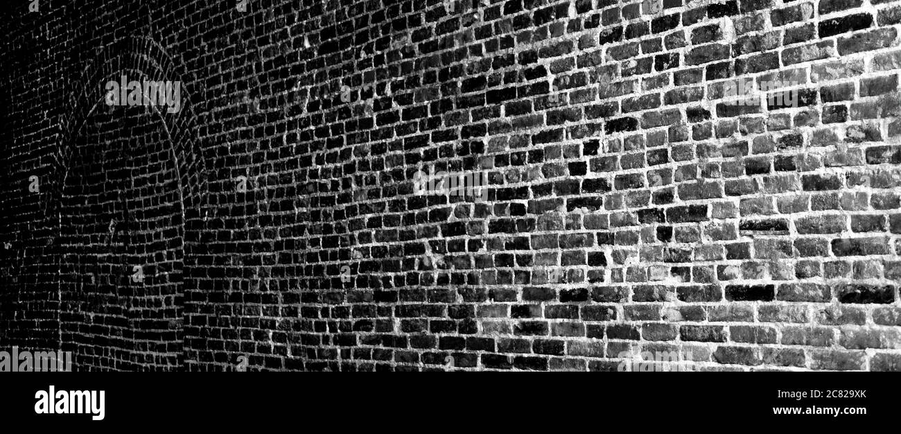 Ein Panorama-Format einer alten Ziegelwand mit gemauerten gewölbten Tür, beleuchtet von dunkel bis hell in alten Keller in schwarz und weiß Stockfoto