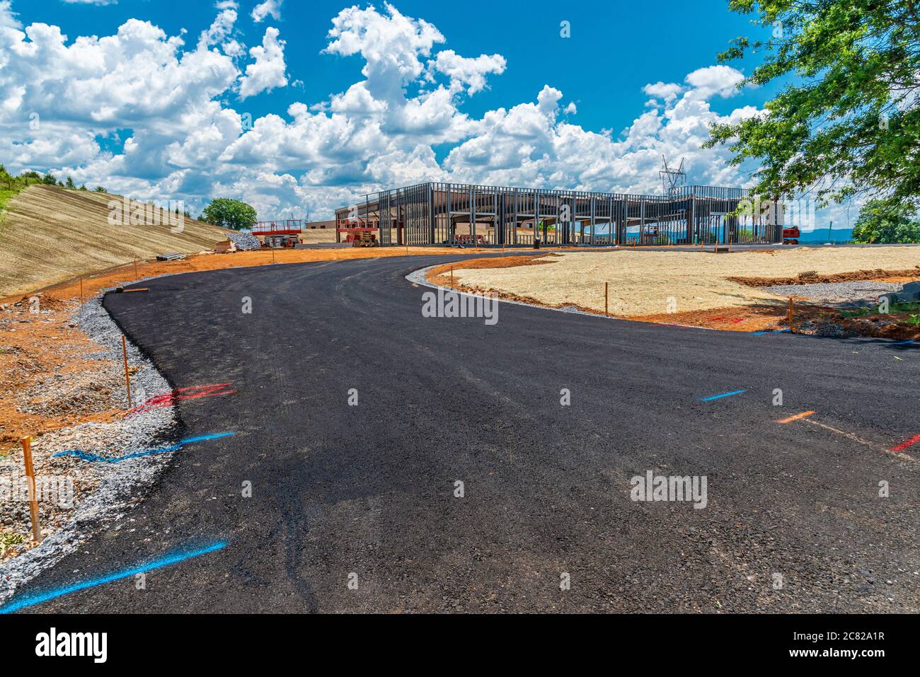 Horizontale Aufnahme einer frischen, auf einer schwarzen Spitze liegenden Straße, die zu einer kommerziellen Baustelle führt. Stockfoto