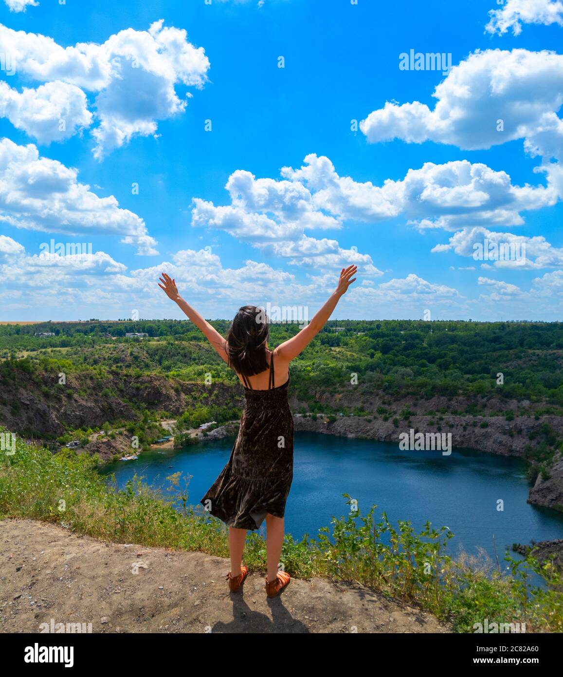 Eine junge Frau mit offenen Händen steht auf einem Hügel über einem malerischen See. Freiheitskonzept. Stock Foto. Stockfoto