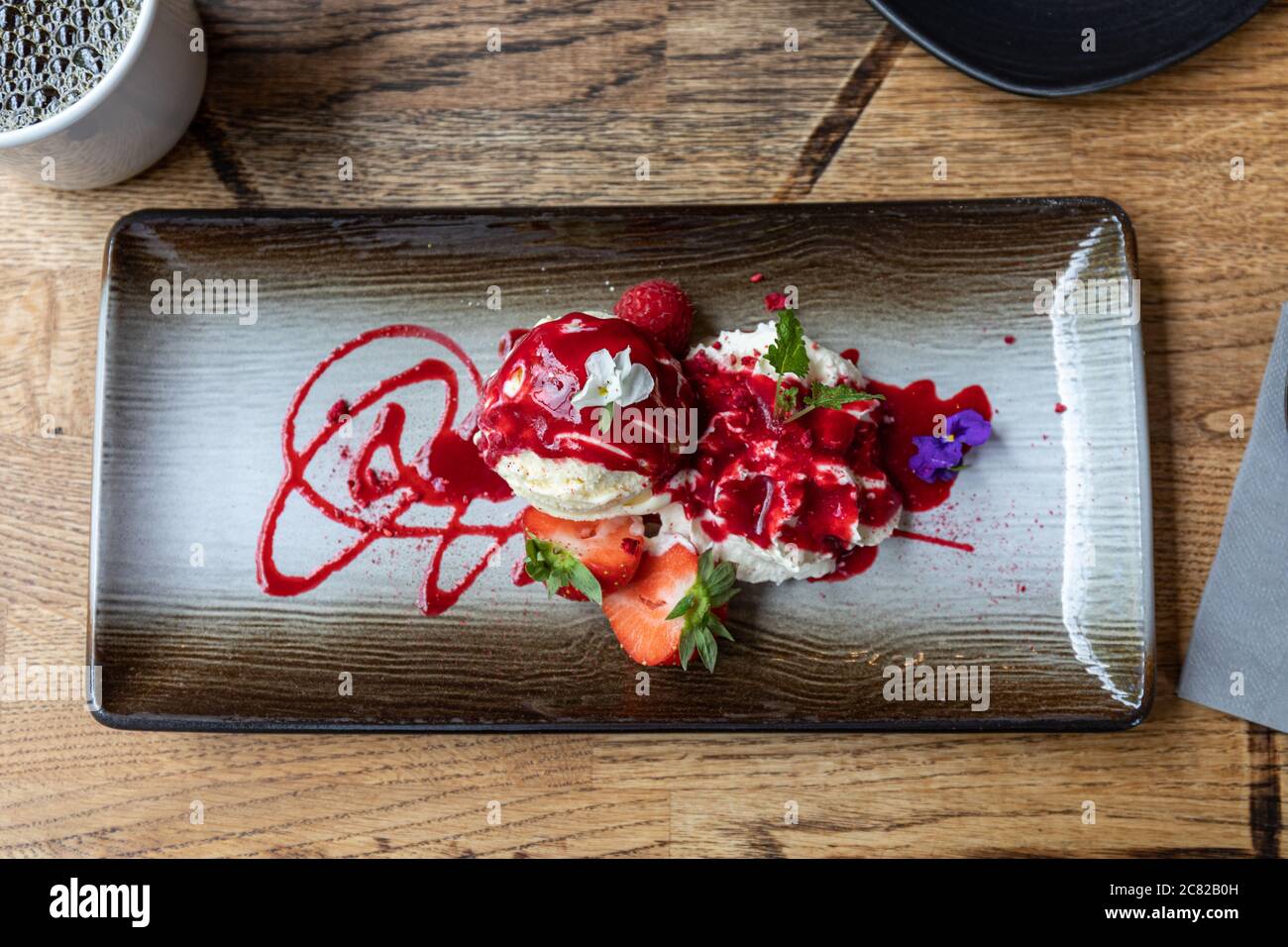 Vanilleeis mit Schlagsahne, Erdbeeren und Himbeersoße Stockfoto