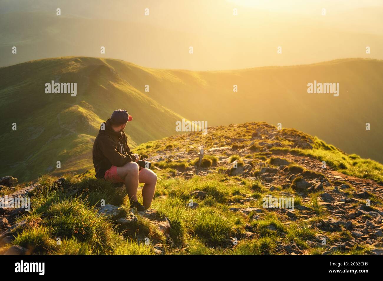 Wunderschöne Berge im Nebel und ein junger Mann sitzt darauf Der Stein Stockfoto