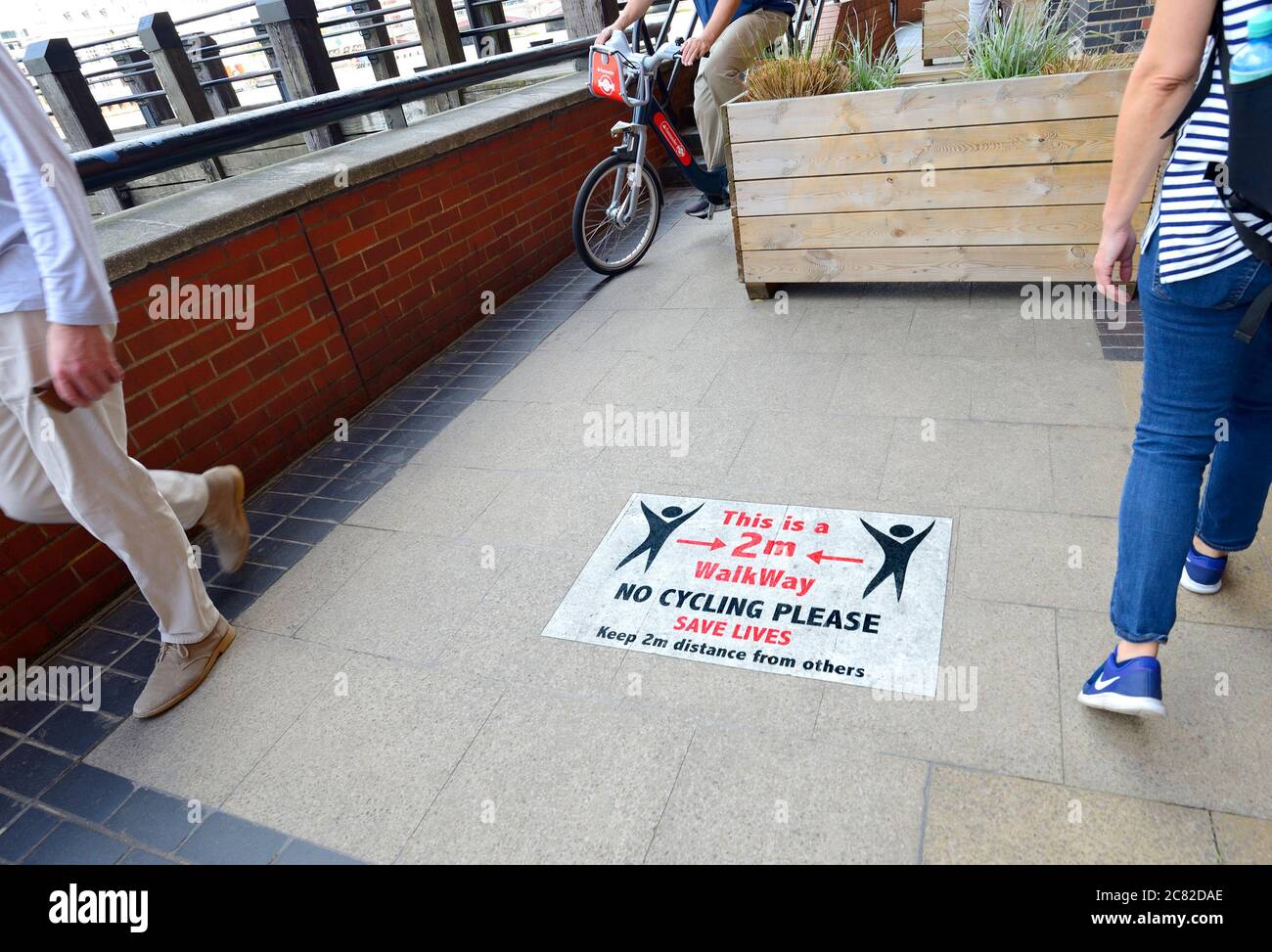 London, England, Großbritannien. COVID-19 Vorsichtsmaßnahmen auf der Südbank. Schilder, die soziale Distanzierung und kein Radfahren - Radfahrer ignorieren die Schilder Stockfoto