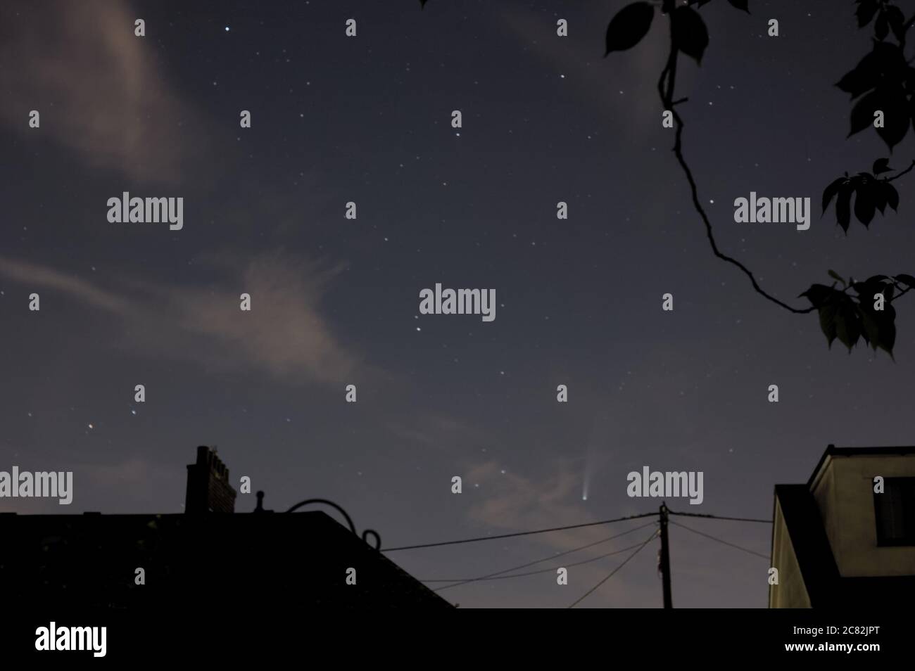 Komet C/2020 F3 NEOWISE, der hellste Komet der letzten Jahre, in einem sternenklaren blauen Stundenhimmel mit Wolkenfetzen über den Dächern von Essex, Großbritannien. Stockfoto
