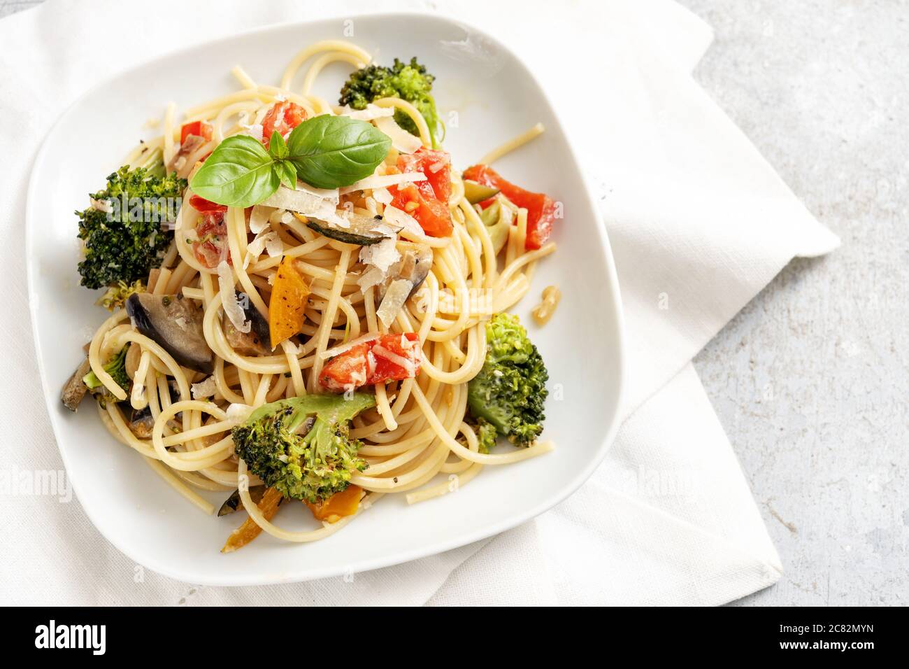 Vegetarische Spaghetti mit Brokkoli, Tomaten, Paprika und Auberginen, gesunde mediterrane Pasta-Mahlzeit auf weißem Teller und hellgrauem Hintergrund, Stockfoto