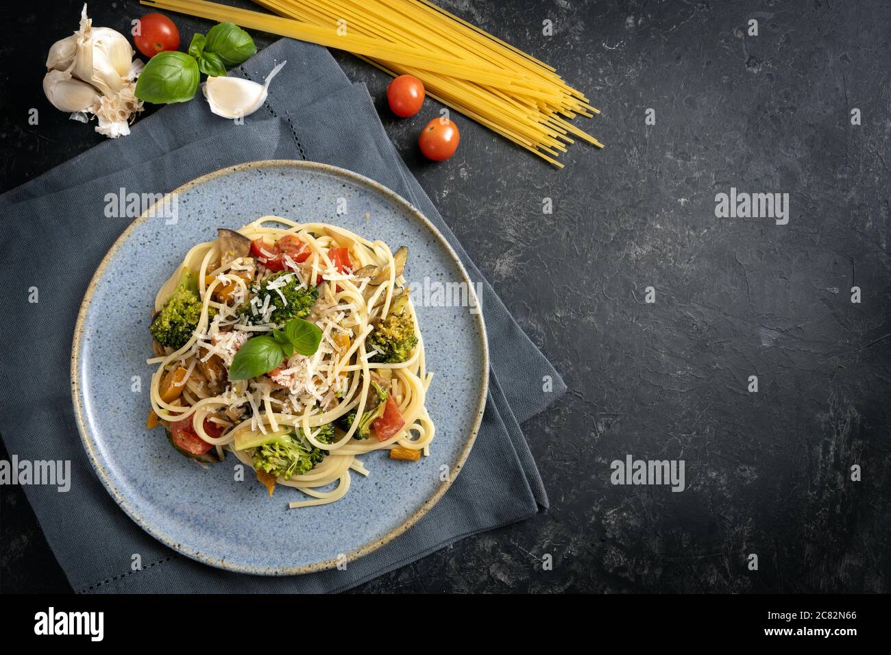 Spaghetti Pasta mit frischem Gemüse und Parmesan-Käse, gesunde vegetarische Mahlzeit und Zutaten auf einem blauen Teller und einem dunkelgrauen rustikalen Hintergrund w Stockfoto