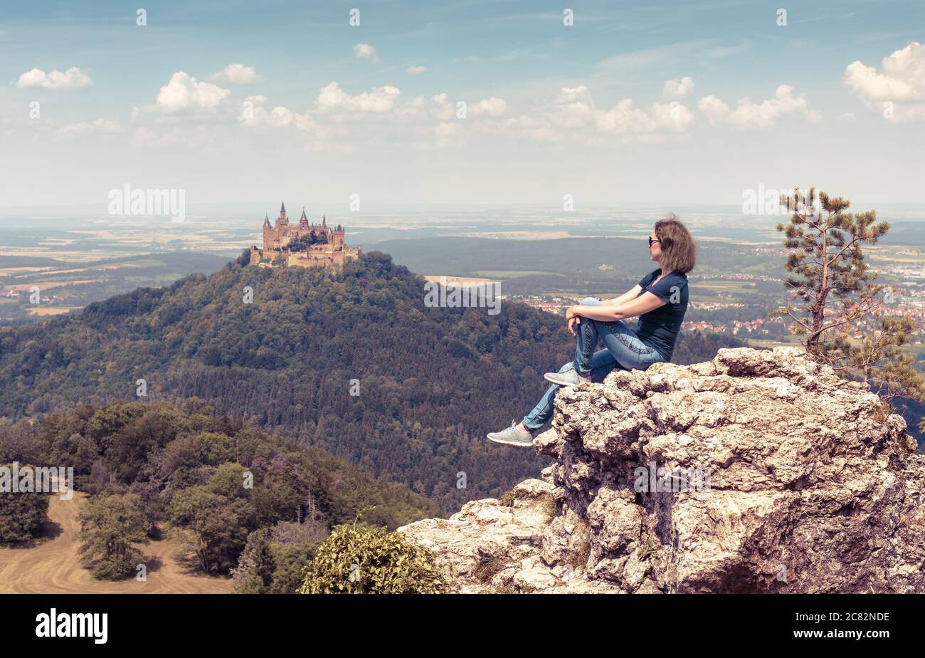 Junge Frau sitzt auf einem Felsen in der Nähe von Schloss Hohenzollern. Dieses gotische Schloss ist Wahrzeichen in der Nähe von Stuttgart. Hübsches Mädchen touristisch reist in moun Stockfoto