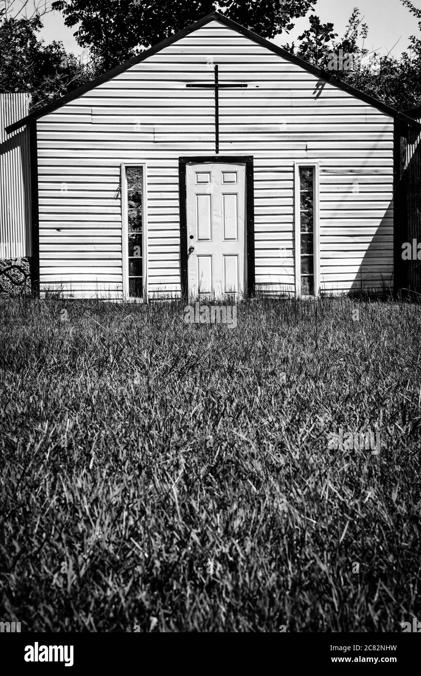 Ein grasbewachsener Vordergrund, eine gefälschte Kirche in Fake Town, einem von Mayberry inspirierten Kunstinstallationskomplex, im ländlichen mittleren Tennessee, USA, in Schwarz-Weiß Stockfoto