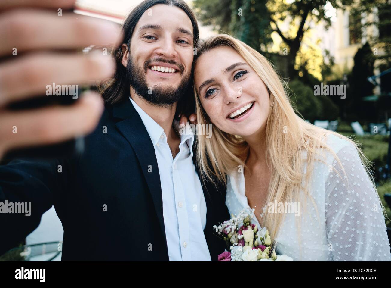 Junge attraktive lächelnde Bräutigam und Braut freudig unter Selfie im Freien Stockfoto