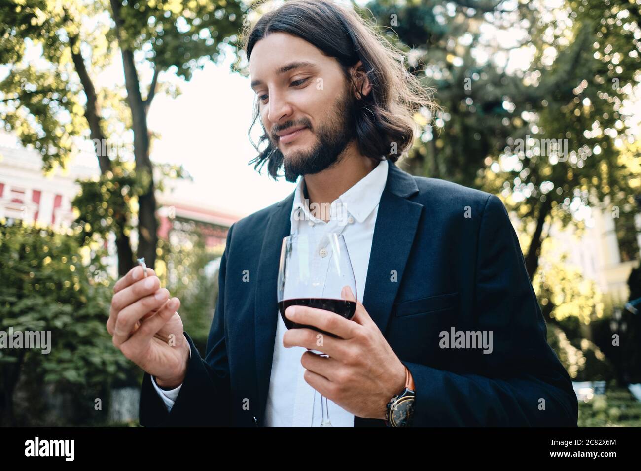 Junger, hübscher bärtiger Mann mit einem Glas Wein, der im Restaurant im Freien einen Trauring hält Stockfoto
