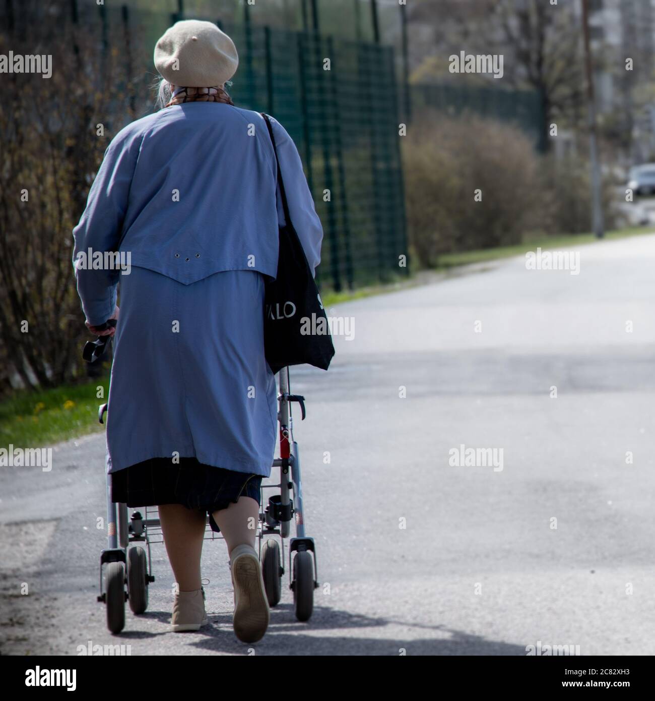 Ältere Frau, die alleine auf einer Straße mit einem Spaziergänger geht Stockfoto