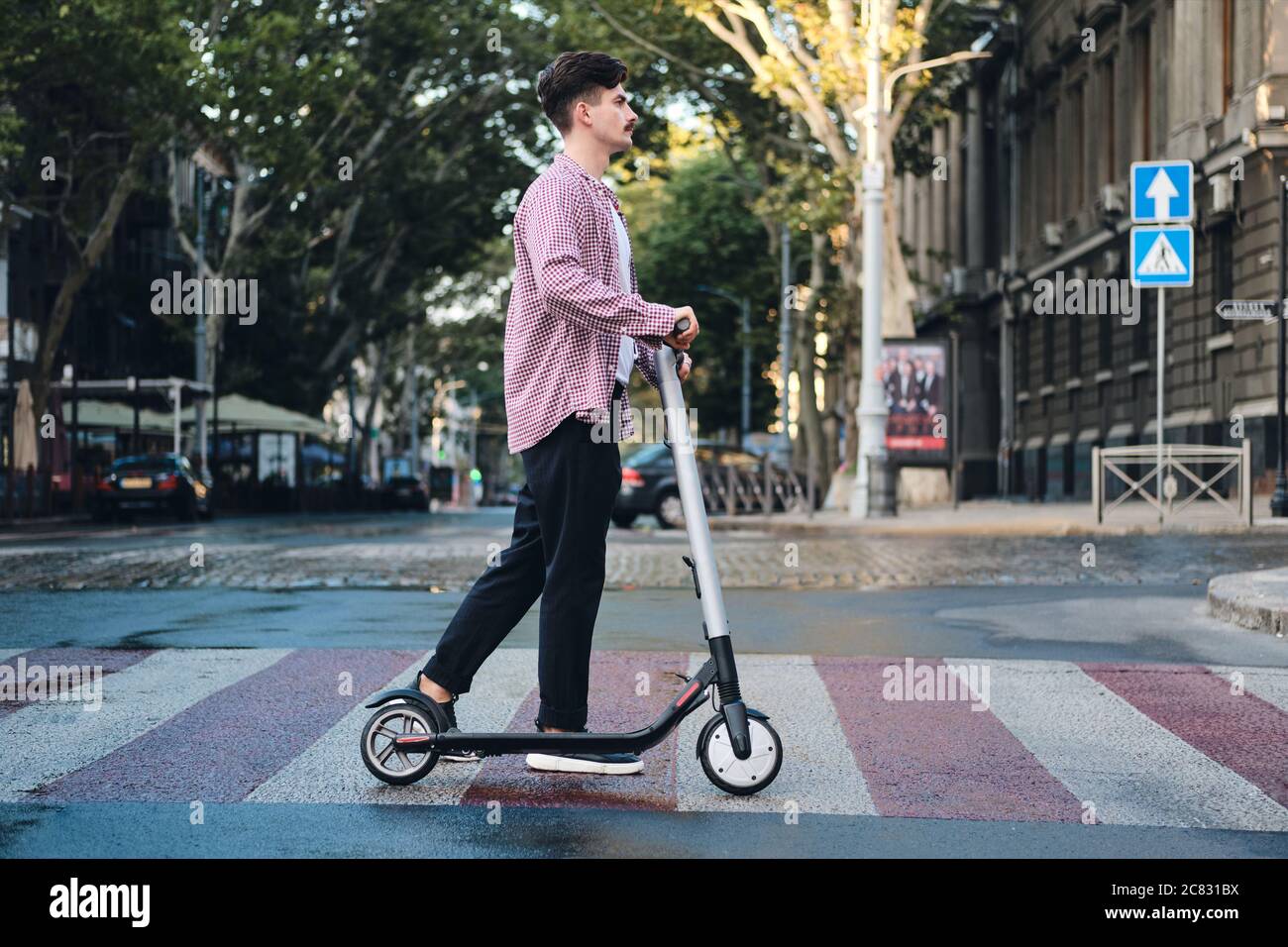 Seitenansicht eines jungen Mannes mit E-Scooter, der auf der Straße auf Fußgängerüberwegen fährt Stockfoto