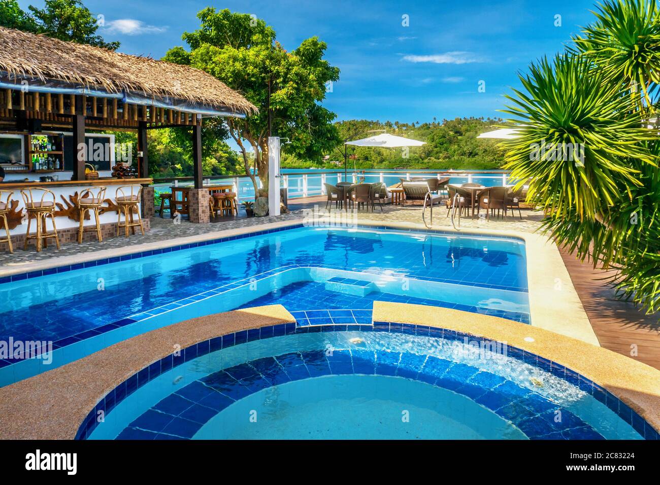 Wunderschöner tropischer Resort Swimmingpool mit lebhaft blauem Wasser und Open-Air Bar mit Strohdach am Wasser, an einem hellen sonnigen Tag. Stockfoto