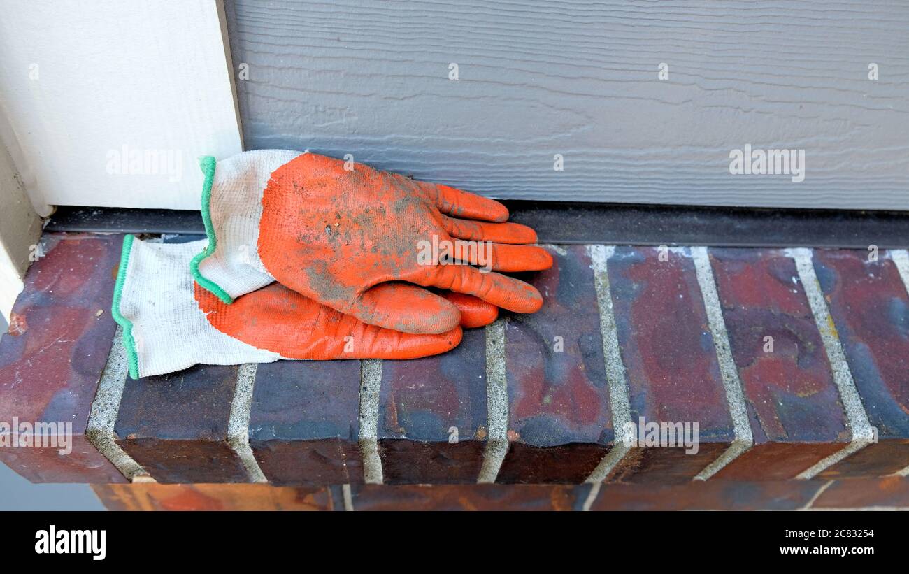Paar orange Garten Arbeitshandschuhe mit Schmutz auf einem Ziegelstein Kante im Freien; gehauchten Schmutz auf Hof Handschuhe für die Gartenarbeit rund um das Haus verwendet. Stockfoto