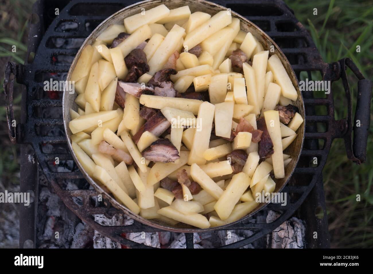 In einer großen Pfanne werden auf offenem Feuer Kartoffeln, Kürbis und Würstchen gekocht Stockfoto