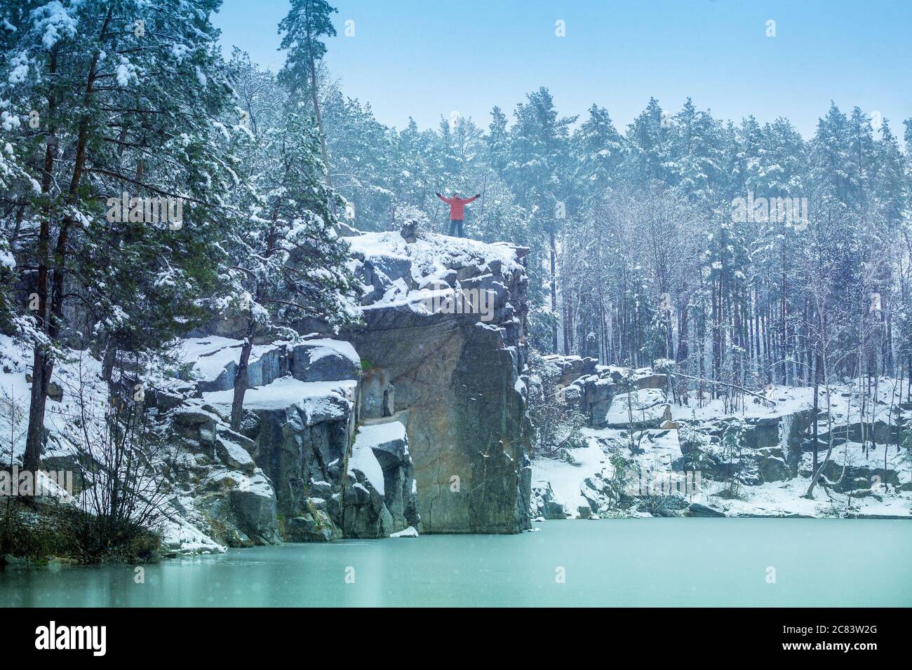 Ein Mann bleibt auf der Klippe am Seeufer mit Schnee im Winter bedeckt und schaut auf den schönen See Stockfoto