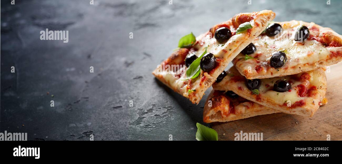 Scheiben gestapelte italienische Pizza auf einer dünnen Kruste mit schwarzen Oliven, Mozzarella und frischen Basilikumblättern in einem Panorama-Banner mit Copyspace für Anzeige gekrönt Stockfoto