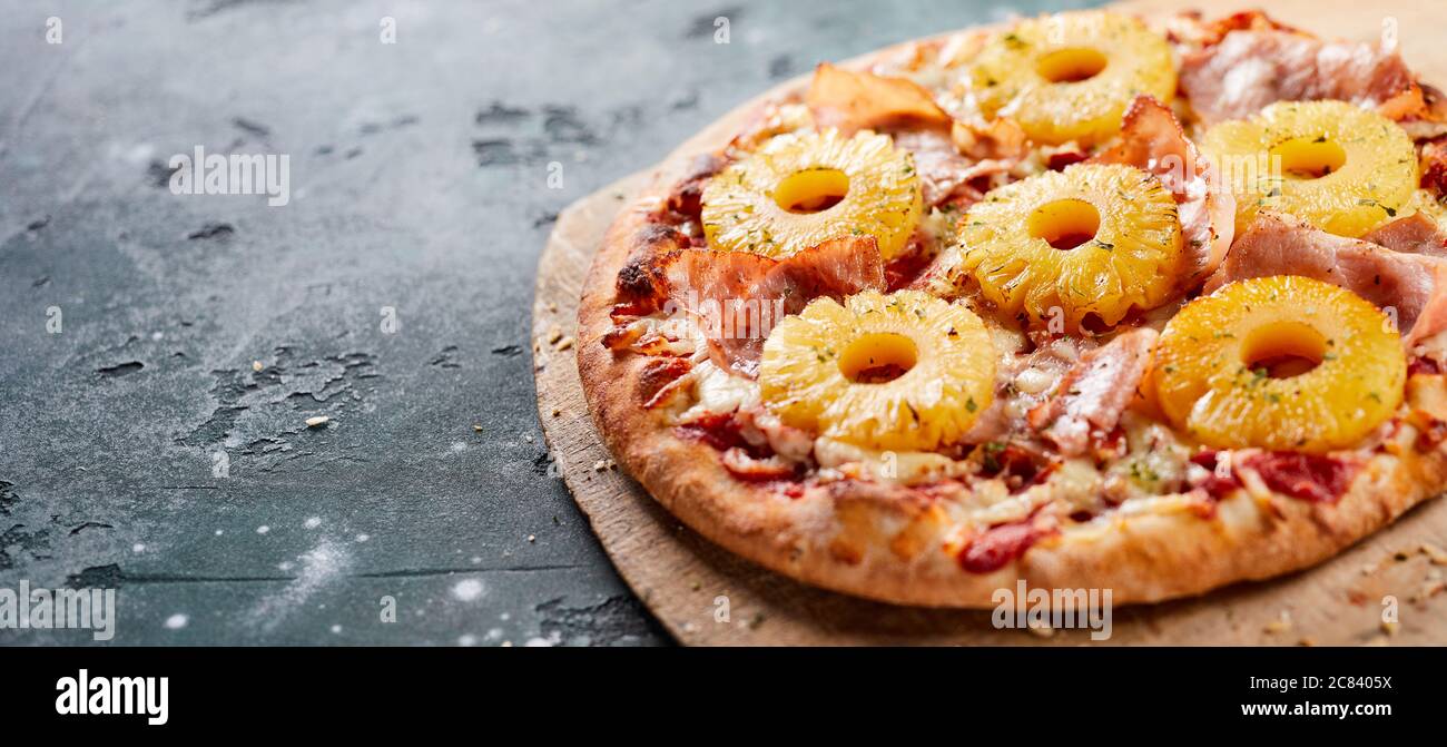 Tropische Hawaii-Pizza mit Ananasscheiben und Schinken auf einer Backplatte aus dem Ofen, serviert auf einem Brett in einem Panorama-Banner mit Copyspace Stockfoto
