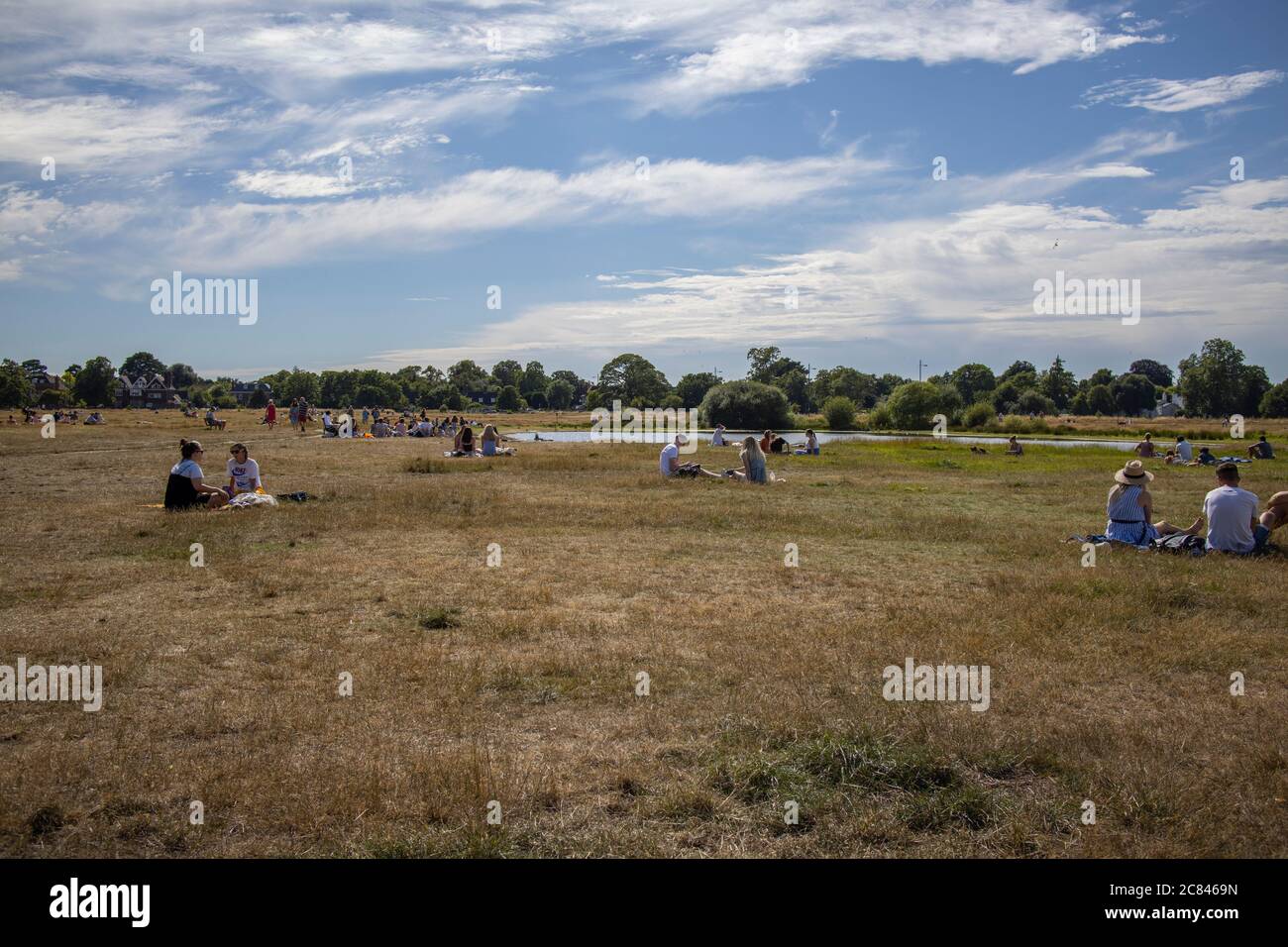 Die Menschen sitzen in der Sonne neben Rushmere Pond, Wimbledon Common, Southwest London, England, Großbritannien Stockfoto