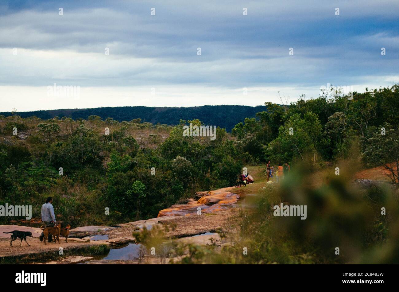 Draufsicht auf eine ruhige Wasserkaskade in Cachoeira das Andorinhas in Ouro Preto Umgeben von Grün, roten Felsen und einer Gruppe von Menschen während eines bewölkten Nachnens Stockfoto