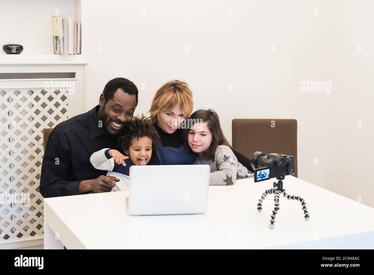 Glückliche multiethnische Familie von Vloggern verwendet einen Computer und einen drahtlos verbundenen Camcorder, um Videos auf ihrem Blog zu senden, gemischt-Rennen Paar mit ch Stockfoto