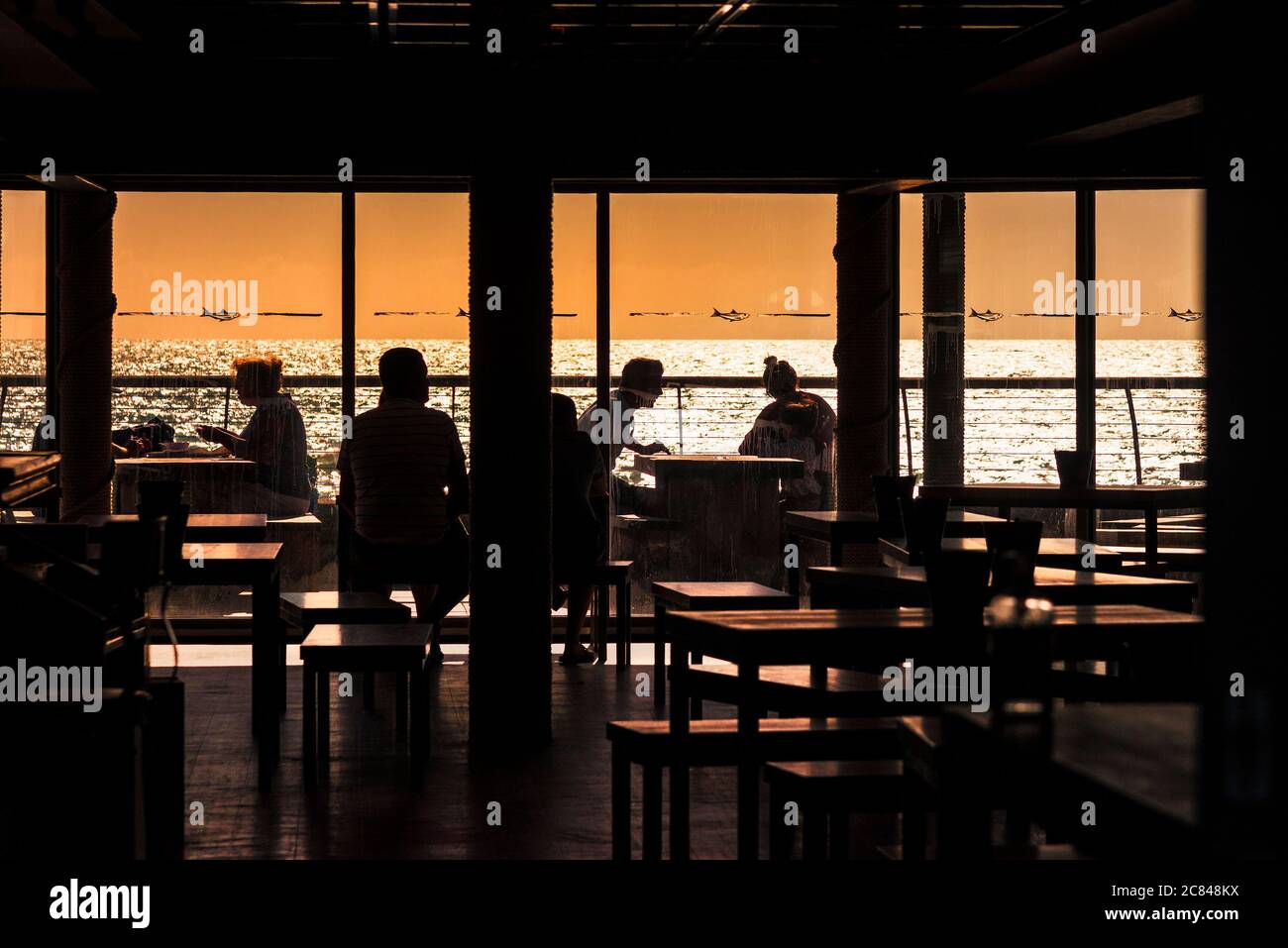 Kunden in Silhouette gesehen sitzen in einem Restaurant mit Blick auf das Meer bei Sonnenuntergang in Fistral in Newquay in Cornwall. Stockfoto