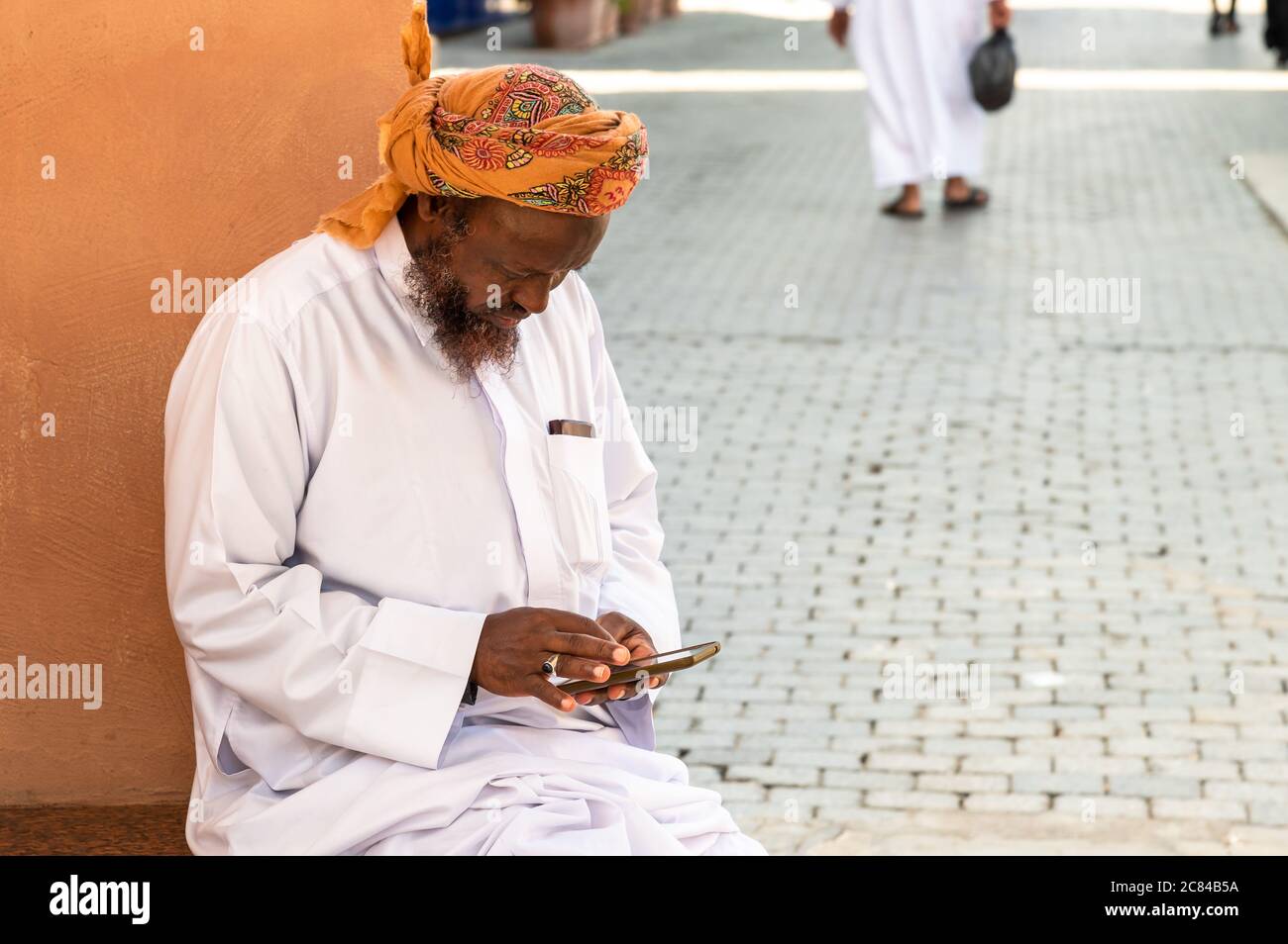 Mutrah, Oman - 10. Februar 2020: Omanischer Erwachsener in traditioneller Kleidung mit Mobile auf der Straße in Mutrah, Sultanat von Oman, Naher Osten Stockfoto