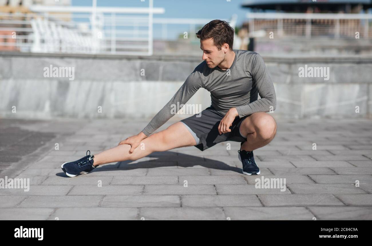 Sportlicher Körper und gesunder Lebensstil. Mann hockt und tut Beinübungen auf der Straße Stockfoto