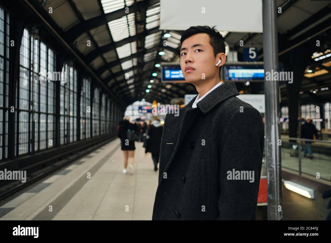 Junger, stilvoller asiatischer Geschäftsmann in schnurlosen Kopfhörern, der am Bahnhof in der Bahn wartet Stockfoto