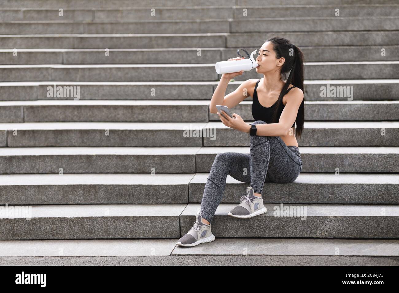Sportliche Asiatische Mädchen Trinkwasser Und Mit Smartphone, Ruhe Nach Dem Training Im Freien Stockfoto