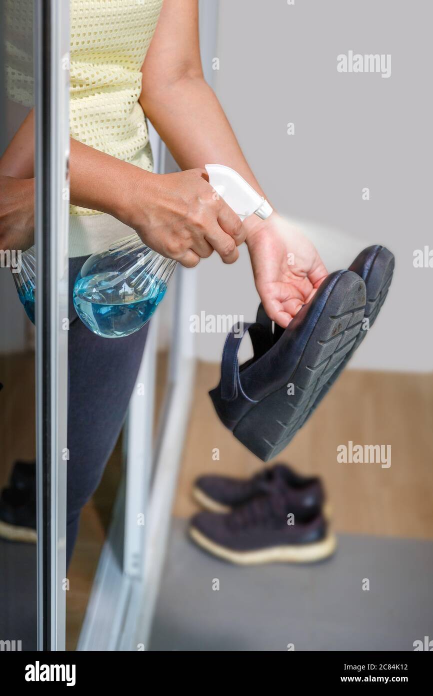 Frau ziehen ihre Schuhe aus und reinigen mit Alkohol, bevor sie ein Haus zum Schutz der infizierten Covid-19 betreten Stockfoto
