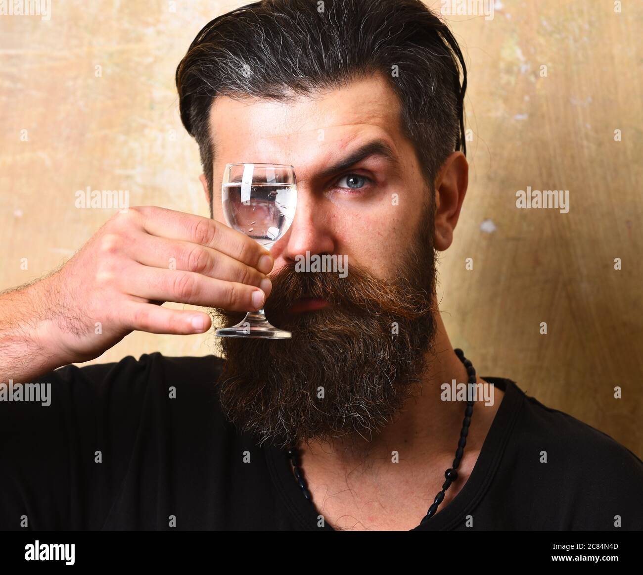 Mann, der durch Wodka in Glas auf beigefarbenem Wandhintergrund schaut. Stockfoto