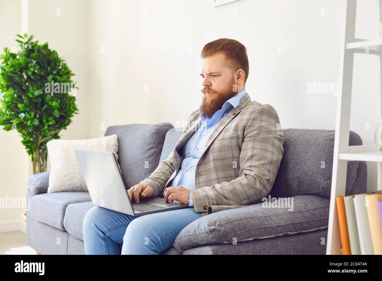 Online im Home Office arbeiten. Lustige dicke Mann arbeitet mit einem Laptop im Apartment-Zimmer. Stockfoto