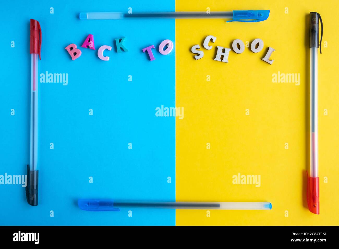 Rahmen aus mehrfarbigen Kugelschreibern auf gelbem und blauem Hintergrund. Inschrift aus farbigen Buchstaben zurück zur Schule. Flach liegend, Platz für Text, Stockfoto