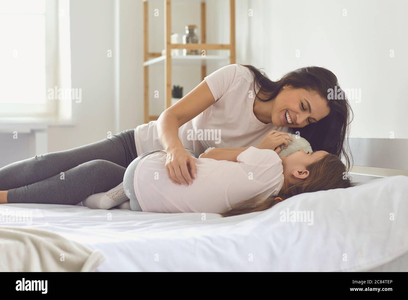 Glückliche Mutter umarmte ihre Tochter auf dem Bett zu Hause. Liebevolle Mama mit Kind zusammen lachen und am Morgen entspannen Stockfoto