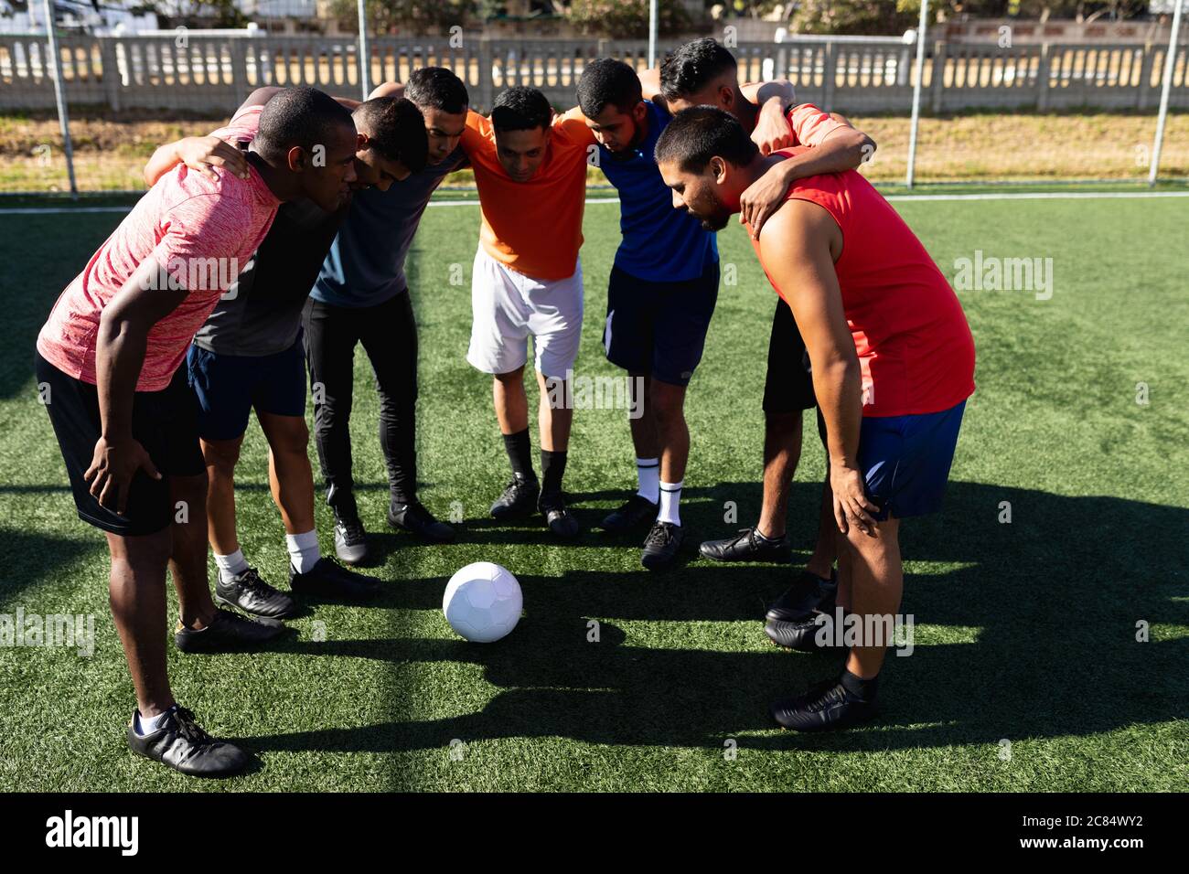 Multi ethnische Gruppe von männlichen fünf ein Seite Fußballspieler tragen Sportkleidung Training auf einem Sportplatz in der Sonne, stehen in Huddle motivierend sein Stockfoto