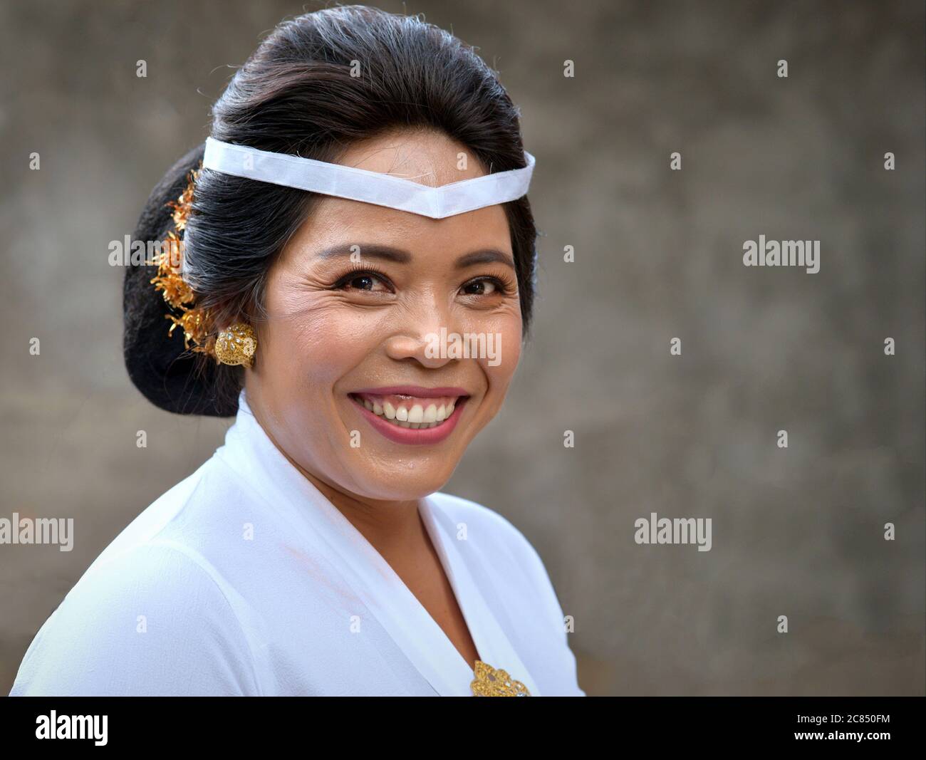Reife indonesische Balinesin trägt weiße Kleidung und lächelt für die Kamera während einer religiösen Hindu-Tempelzeremonie (Odalan-Festival). Stockfoto