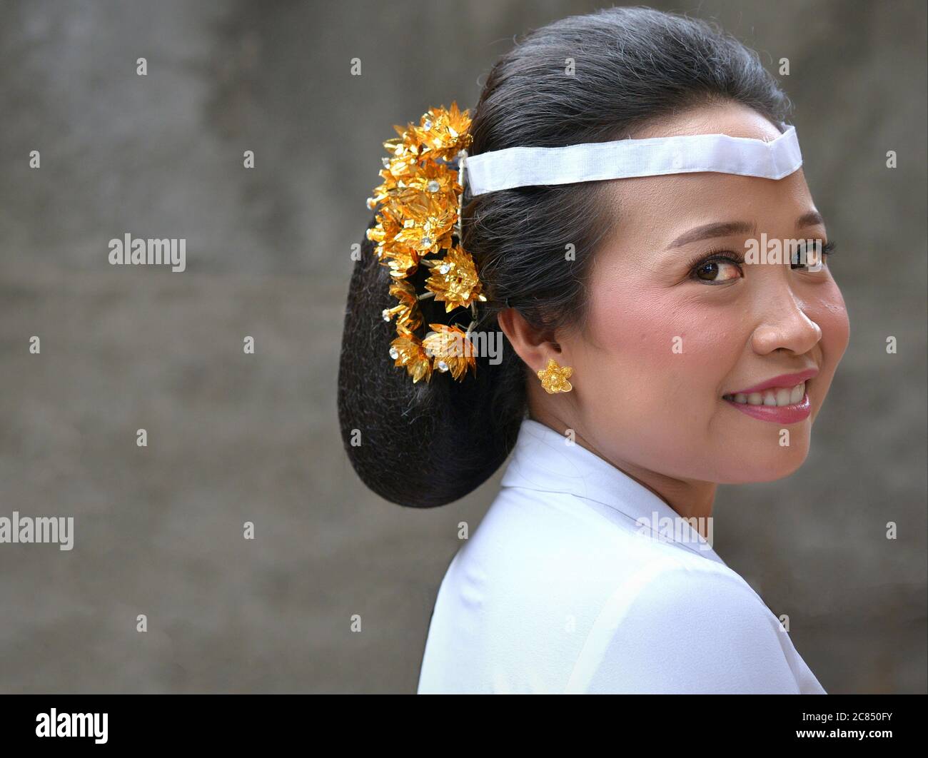 Junge indonesische Balinesin trägt weißes Outfit und lächelt während einer religiösen Hindu-Tempelzeremonie (Odalan-Festival) für die Kamera. Stockfoto