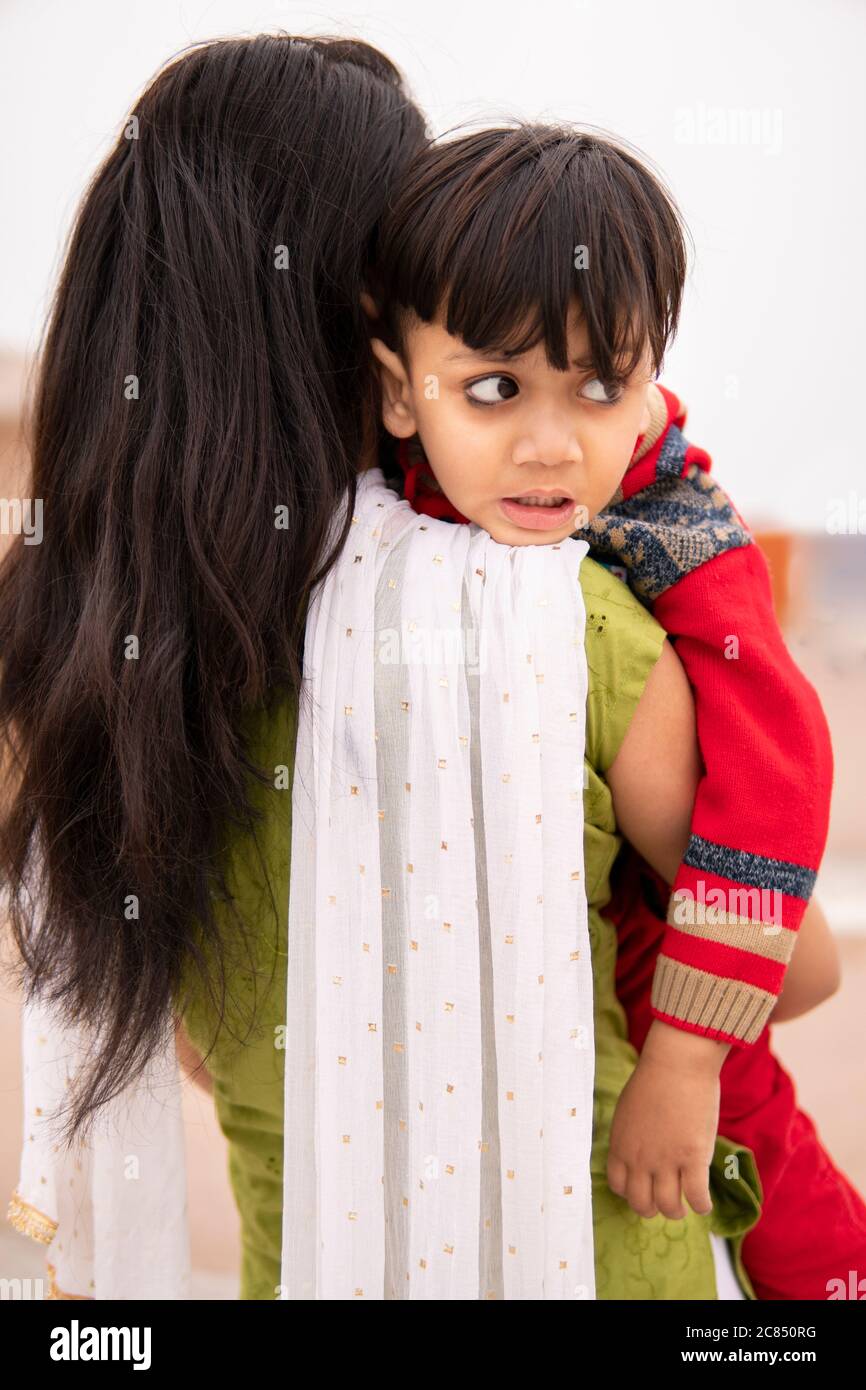 Rückansicht einer Tante, die ihren geschnittenen kleinen Neffen im Freien hält. Sie trägt traditionelle indische Kleidung Salwar Kameez und Dupatta. Stockfoto