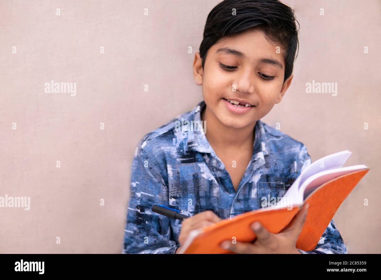 Kleiner indischer Junge Student, der zu Hause studiert. Er schreibt auf Notizbuch und macht seine Hausaufgaben. Stockfoto