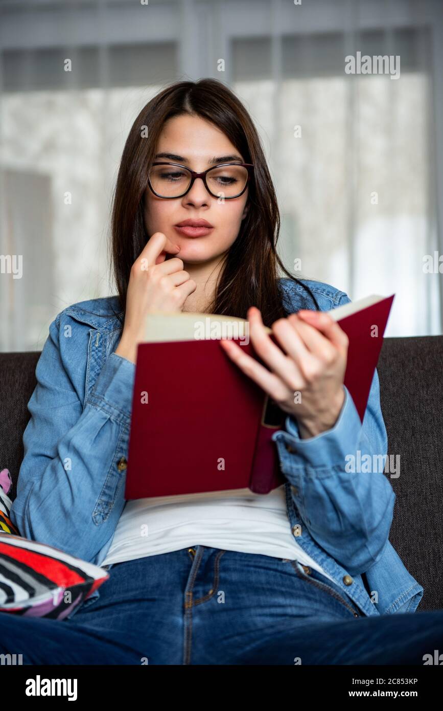 Entspannte glückliche Frau, die ein Buch liest, sitzt auf einer Couch zu Hause. Entspannte glückliche Frau, die ein Buch liest, sitzt auf einer Couch zu Hause. Stockfoto