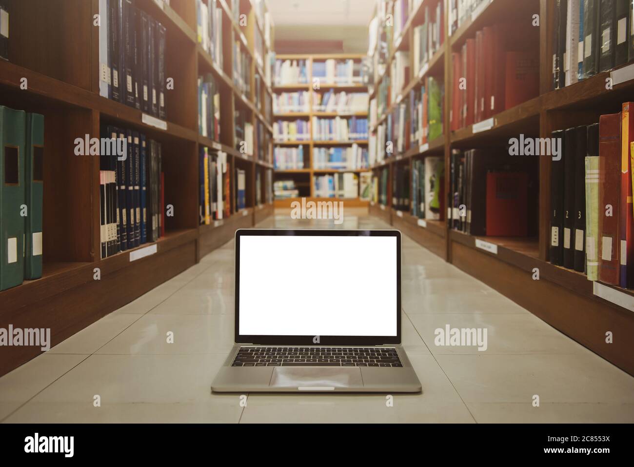 Laptop mit leerem Bildschirm auf dem Boden. Innenhintergrund, Bücherregal, Bibliothek.Educational Technology Konzept. Stockfoto