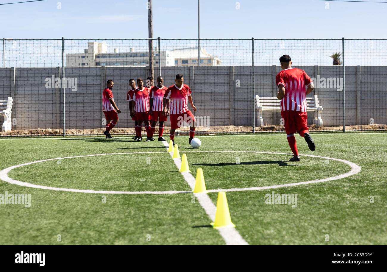 Multi ethnische Team von männlichen fünf ein Seite Fußballspieler tragen eine Mannschaftsstreifen Training auf einem Sportplatz in der Sonne, Aufwärmen Tackling mit Ball betwe Stockfoto