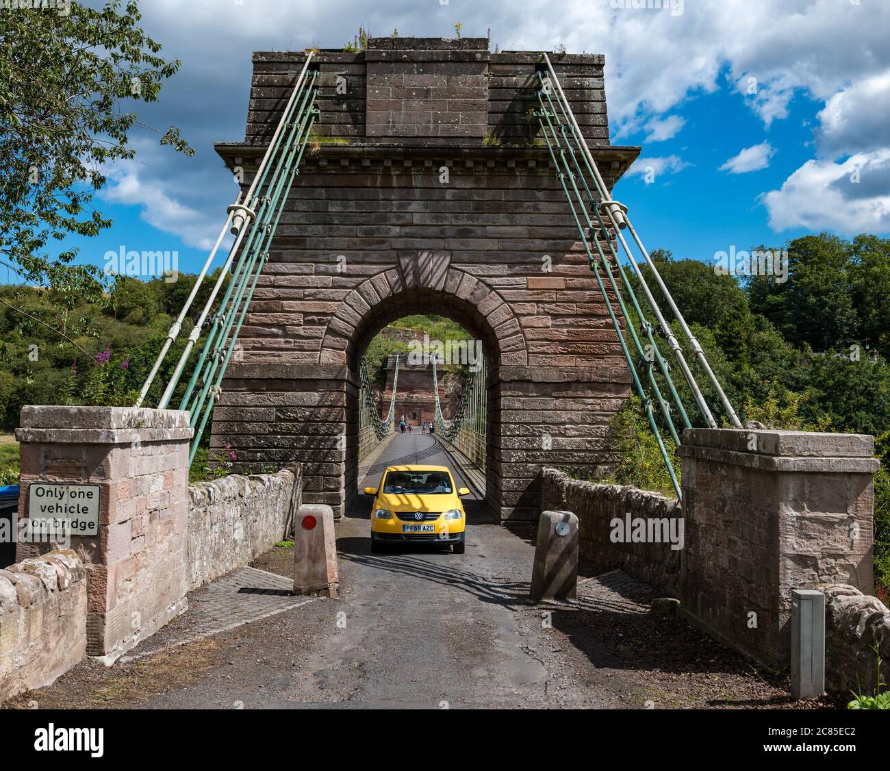 River Tweed, Englisch/Schottische Grenze, Großbritannien, 21. Juli 2020. 200 Jahre Union Bridge: Die Brücke feiert am 26. Juli ihr 200-jähriges Bestehen. Es war die erste Auto-Hängebrücke in Großbritannien. Zum Zeitpunkt ihrer Errichtung war sie mit 137 m die längste schmiedeeiserne Hängebrücke der Welt. Es wird immer noch regelmäßig von Fußgängern, Radfahrern und Autos verwendet, aber Autos müssen es zu einer Zeit überqueren. Diese Ansicht stammt von der schottischen Grenze. Ein gelbes Auto überquert die Brücke Stockfoto